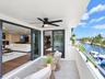 Covered balcony featuring oversized neutral floor tiles, a matte black ceiling fan with integrated lighting, and dark-framed sliding glass doors