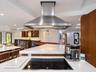 Kitchen featuring a white solid-surface countertop with an integrated electric cooktop, a stainless steel chimney-style range hood, and wood-finish ca
