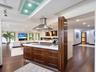 Kitchen island with dark wood-finish cabinetry, solid surface countertop, stainless steel cooktop, and stainless steel chimney range hood