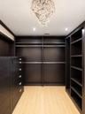 Custom walk-in closet featuring dark wood-finish built-in cabinetry, floor-to-ceiling shelving, integrated hanging rods, a central dresser unit with m