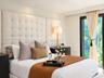 Tufted floor-to-ceiling fabric headboard, recessed ceiling lighting, and floor-to-ceiling window with dark-frame trim