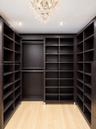 Custom dark-finish built-in shelving, wood-finish flooring, integrated metal hanging rods, and a tiered crystal chandelier
