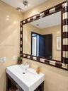 Rectangular white vessel sink atop a dark wood-finish vanity, large wall mirror with a decorative two-tone wood and metal frame, and full-height stone