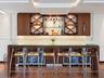 Custom built-in bar featuring wood cabinetry, integrated glass shelving with X-frame detailing, under-cabinet lighting, and a glass-top counter with m