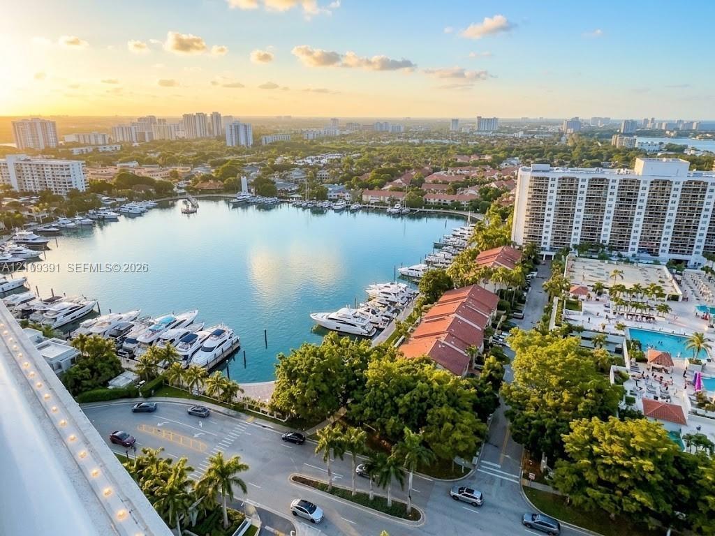 Aerial perspective of a coastal community featuring a deep-water marina, multiple high-rise structures, a private swimming pool, and established tropi