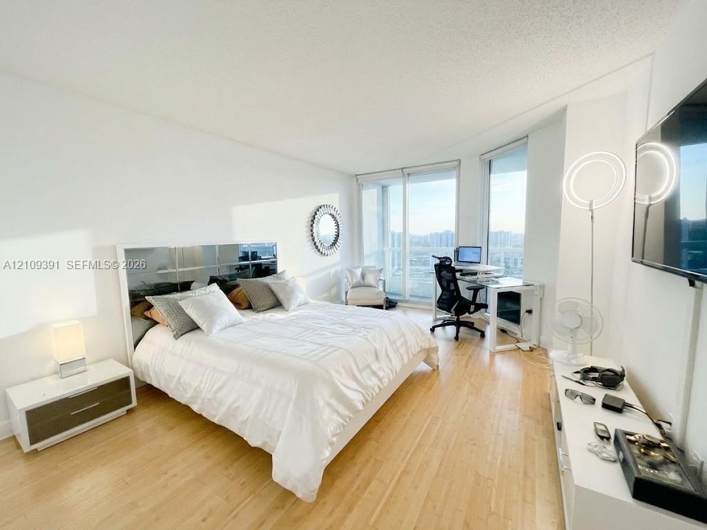 Floor-to-ceiling windows, light-toned wood-finish flooring, and crisp white walls