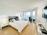 Floor-to-ceiling windows, light-toned wood-finish flooring, and crisp white walls