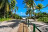 Sandy path featuring a wooden boardwalk, metal railings with rope accents, mature palm trees, and coastal water access
