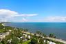 Elevated coastal scenery featuring an expansive shoreline, dense palm tree clusters, manicured green space, and open water horizon