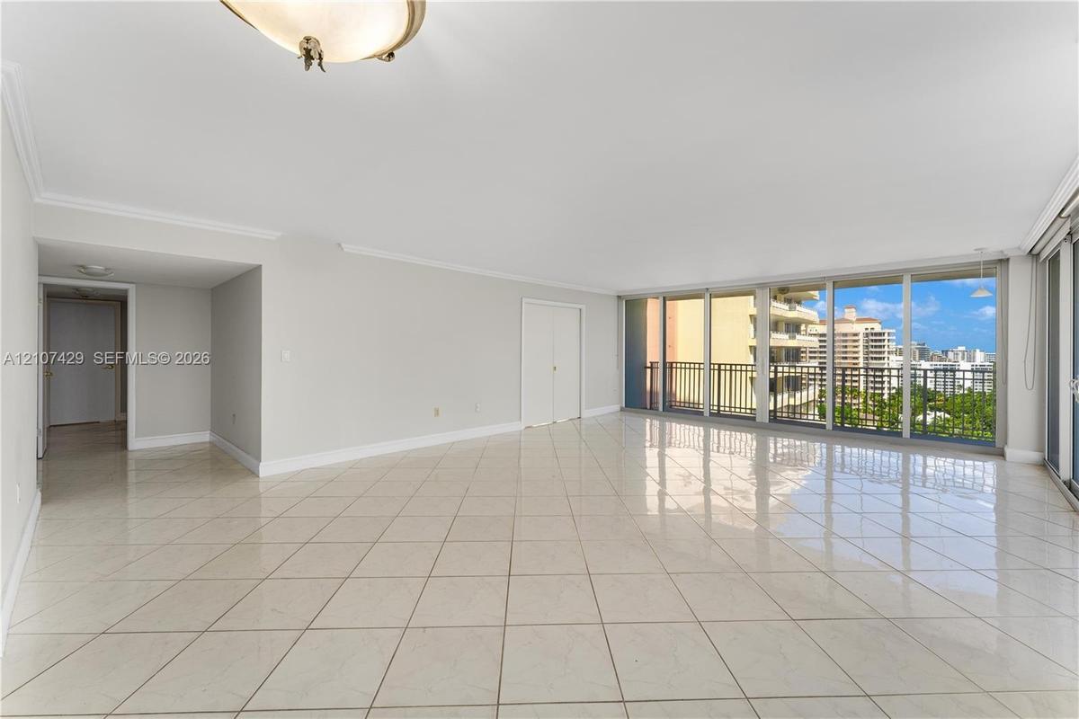 Spacious room featuring light-toned tile flooring, floor-to-ceiling glass sliding doors, and a metal balcony railing
