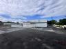 Commercial structure featuring a white exterior, expansive asphalt parking area, covered entrance, and perimeter fencing