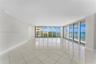Expansive interior space featuring large-format tile flooring, crown molding, and floor-to-ceiling glass panel walls with access to a balcony