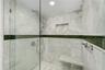 Walk-in shower featuring large-format stone tile, a built-in bench, a glass enclosure, an integrated wall niche, and a contrasting green glass tile ac