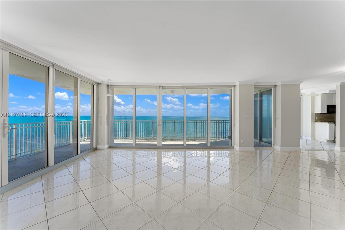 Floor-to-ceiling glass doors, expansive balcony with metal railing, polished tile flooring, and neutral wall finishes
