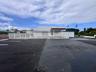 Commercial exterior featuring a paved parking lot, metal perimeter fencing, covered entryway, and white stucco facade