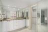 Dual vanity featuring white cabinetry, stone-surface countertops, metallic hardware, recessed lighting, and expansive wall-to-wall mirrors