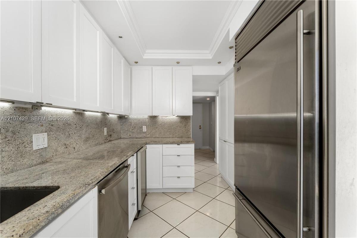 Kitchen featuring white shaker-style cabinetry, stone countertops, stainless steel appliances, under-cabinet lighting, and tile flooring