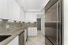 Kitchen featuring white shaker-style cabinetry, stone countertops, stainless steel appliances, under-cabinet lighting, and tile flooring