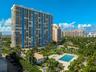 High-rise residential tower featuring private balconies, an inground swimming pool, sprawling landscaped grounds, and mature palm trees