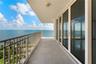 Covered balcony with concrete flooring, full-length sliding glass doors, and metal railing overlooking the ocean