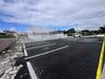 Asphalt-paved parking area featuring marked spaces, concrete parking bumpers, a perimeter metal fence, and an exterior structure with a covered entran