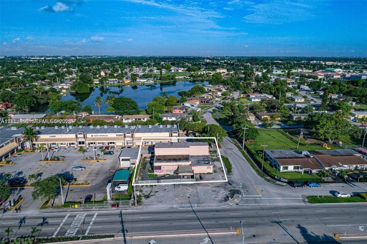 Aerial perspective of a corner commercial property featuring direct street access, a paved parking lot, and proximity to a regional waterway