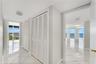 Interior hall featuring white tile flooring, floor-to-ceiling louvered closet doors, and multiple entryways showcasing direct water and shoreline scen