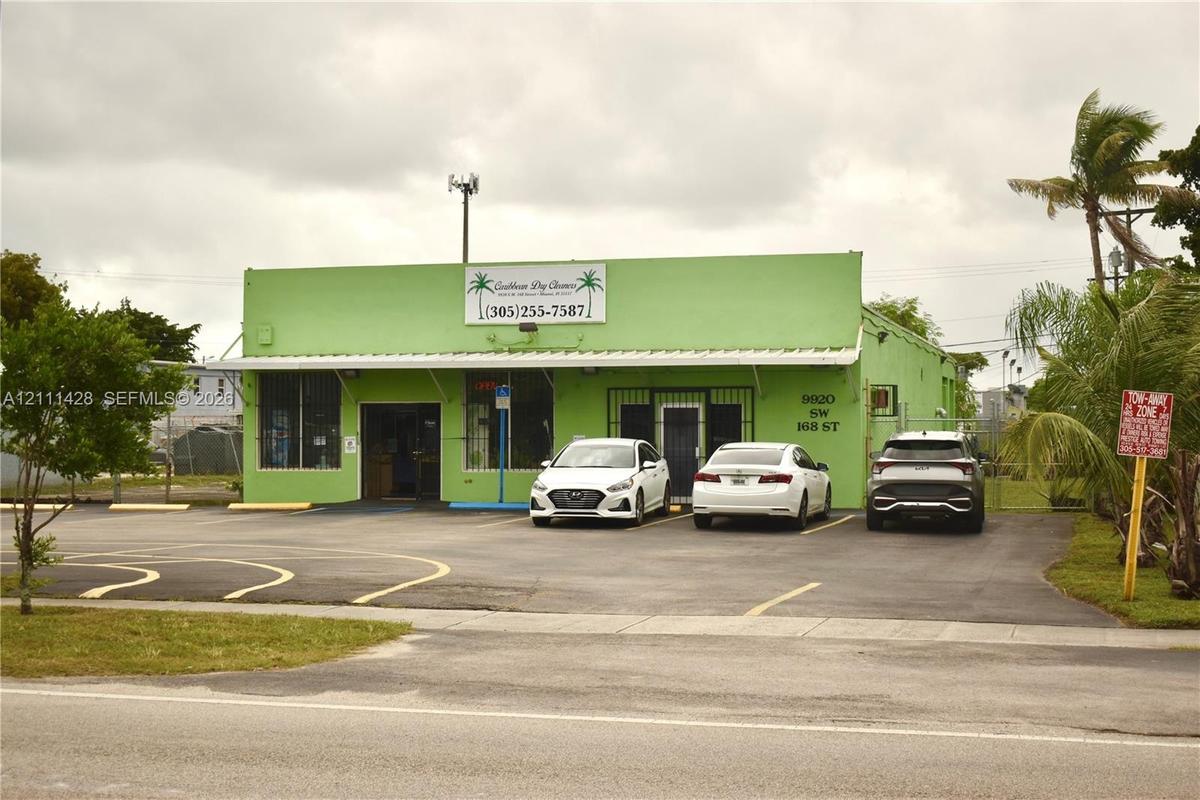 Commercial property featuring a concrete exterior, metal roof canopy, and asphalt parking area