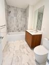 Bathroom featuring large-format tile flooring, wood-finish vanity with a rectangular sink, wall-mounted mirror, and a tile-surround soaking tub with a