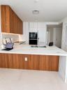 Modern kitchen featuring a waterfall-edge stone countertop, wood-finish cabinetry, built-in wall oven, undermount sink with a gooseneck faucet, and la