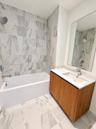Bathroom featuring a wood-finish vanity with an integrated rectangular sink, stone-composite countertop, full-width wall mirror, and porcelain tile fl