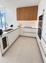 Modern kitchen featuring flat-panel cabinetry with wood-finish uppers, large-format tile flooring, stone-composite countertops, under-cabinet lighting