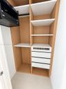 Custom closet featuring wood-finish cabinetry, white shelving, four integrated drawers, and a built-in electronics rack