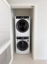 Stacked laundry center featuring a high-efficiency front-load washer and dryer set, housed within a closet with louvered bi-fold doors