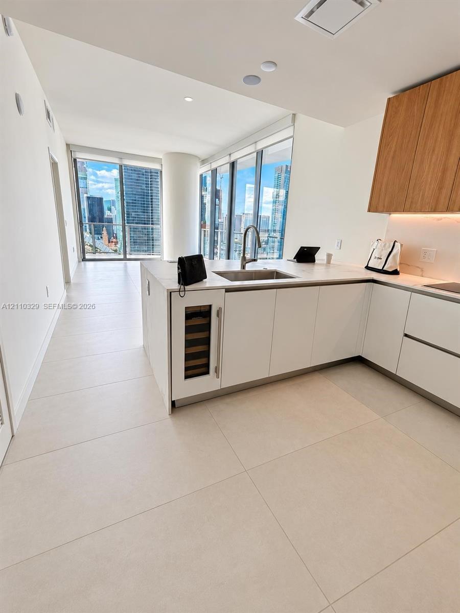 Kitchen featuring custom cabinetry with white lower and wood-finish upper units, integrated wine refrigerator, quartz-surface countertops, and expansi