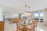 Dining area featuring large-format stone tile flooring, floor-to-ceiling mirror wall, rectangular crystal chandelier, and sliding glass doors with dir