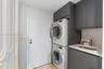 Laundry area featuring charcoal-toned cabinetry, light-toned stone-finish countertop, integrated sink with a gooseneck faucet, and stacked appliance u