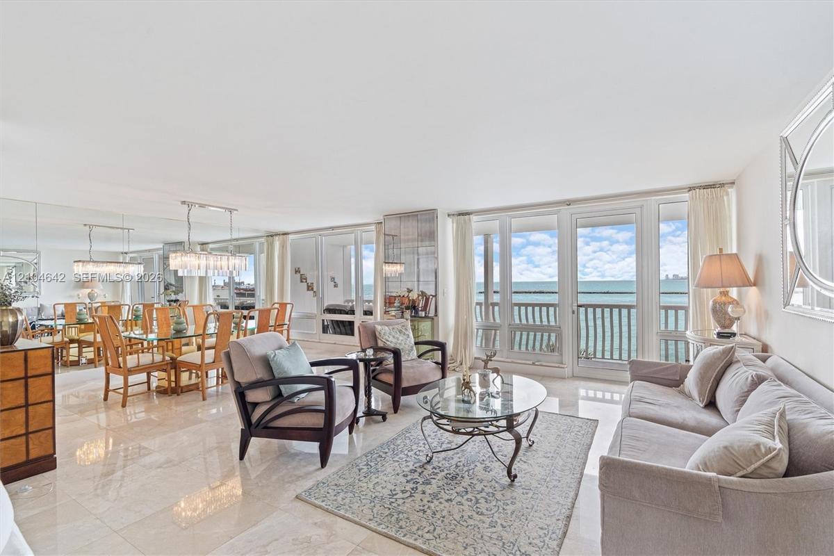 Open-concept living space featuring polished stone flooring, floor-to-ceiling glass paneling, a full-wall mirror, and a balcony with direct water expo