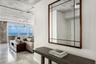 Exposed concrete ceiling, floor-to-ceiling glass paneling, stone-finish flooring, white flat-panel cabinetry, and a center island with a built-in wine