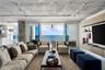 Exposed concrete ceiling with industrial track lighting, floor-to-ceiling glass doors, wall-mounted light wood-finish cabinetry, and balcony access fe