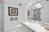 Vanity featuring a light-toned wood-finish cabinet and stone-surface countertop with an integrated basin, large wall-mounted mirror, geometric tile sh