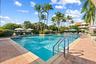 Swimming pool featuring a paver stone deck, metal entry handrails, and surrounding mature palm trees