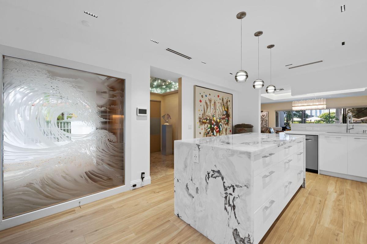 Kitchen featuring a large central island with natural stone waterfall countertops, wood-finish flooring, custom pendant lighting, and a decorative gla