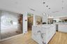 Kitchen featuring a large central island with natural stone waterfall countertops, wood-finish flooring, custom pendant lighting, and a decorative gla