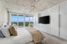 Exposed concrete ceiling with industrial-style track lighting, expansive floor-to-ceiling glass sliding doors, private balcony, and ocean backdrop
