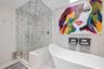 Freestanding soaking tub, glass-enclosed walk-in steam shower with geometric patterned tile, and polished natural stone wall surfacing. Newly remodele