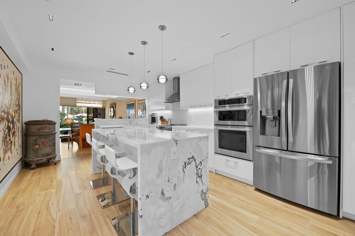 Kitchen featuring a waterfall island with stone countertop, stainless steel appliances, flat-panel cabinetry, wood-finish flooring, and recessed light