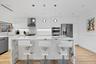 Kitchen featuring a waterfall-edge stone island, high-gloss cabinetry, stainless steel appliances, recessed ceiling lighting, and wood-finish flooring