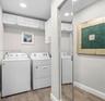 Laundry space featuring white shaker-style wall cabinetry, recessed ceiling lighting, and wood-finish flooring