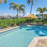 In-ground swimming pool featuring tile coping and stone paver decking, surrounded by mature palm trees and established hedging